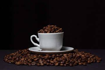 Coffee beans on a black background. A coffee cup full of coffee beans. Large serving of caffeine