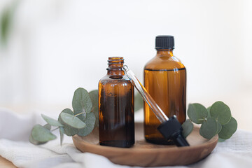 Essential oils in glass dark bottle. Skin and body care treatment concept. Eucalyptus branch.