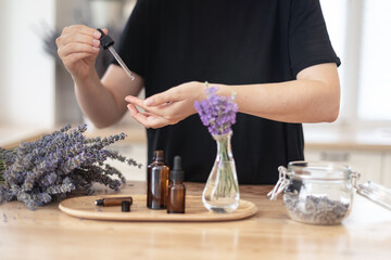 Essential oils of lavender in a glass dark bottle. The girl cares for the skin and hair. Scandinavian interior.