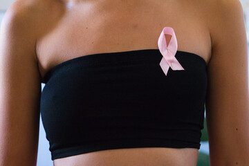 detail of black top and pink ribbon against cancer on the breast of a woman who has undergone...