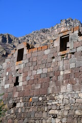 The old stone wall of the monastery. Windows without glass. View of the mountains and the sky without clouds.