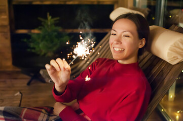 Obraz na płótnie Canvas Young happy girl with sparkler in the evening on the terrace of the house. Holiday christmas and new year. defocus