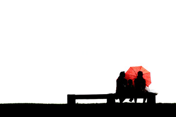 Fototapeta na wymiar Silhouette of parents with child behind umberella sitting on bench