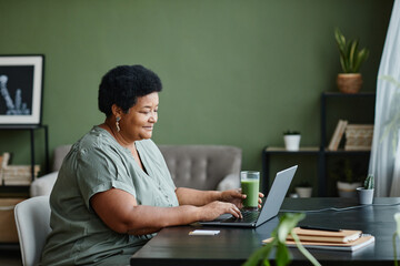 Side view portrait of black senior woman using laptop at home and smiling, copy space