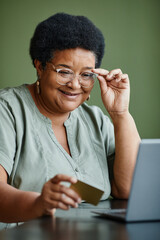 Vertical portrait of black senior woman holding credit card and shopping online from home
