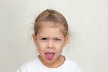 Isolated caucasian funny little girl of 5 years looking at camera and sticking out tongue with suspicion on white background