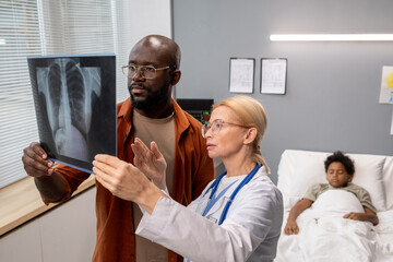 Obraz premium Female doctor showing the x-ray image of lungs to the father, and they discussing the disease together at hospital
