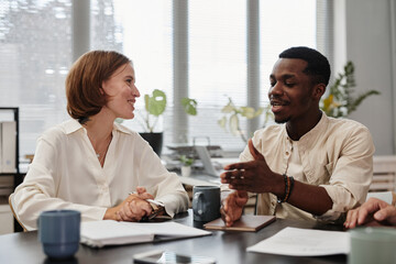 African businessman talking to young businesswoman at the table during a meeting at office