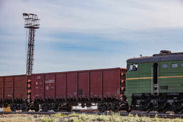 Ore loading station. Open wagons and locomotive with machinist (operator) right. Lighting mast left. Blue sky, clouds. Khromtau, Kazakhstan. 
