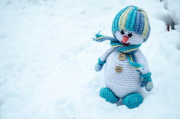 Snowman in a hat and scarf crocheted sitting on the snow Christmas photo handmade toy.