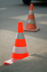 Two safety cones on asphalt road. New cone on front in focus, old on background blurred.