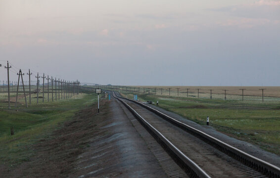 View of railroad in Kazakhstan steppe, near Arkalyk. Perspective of rails and electric poles. Title on sign: Locomotive stop.