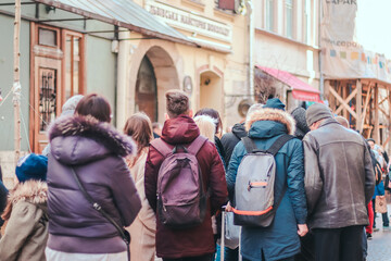 Anonymous crowd of people stand in line at a store, a mall during a pandemic, walking down a city street. Tourists travel to Europe. Back view