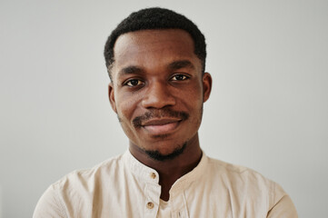 Portrait of African young man dressed in shirt looking at camera against the white wall