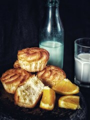 rustic still life with cupcakes, slices of orange, bottle of milk and glass with milk and selective focus