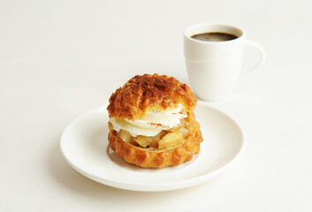 Shu cake dessert with cream on a white plate and a cup of coffee. White background