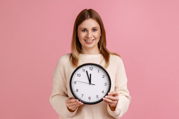 Portrait of happy positive blond woman holding big wall clock, looking at camera with pleasant...