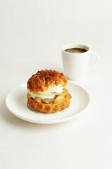 Shu cake dessert with cream on a white plate and a cup of coffee. White background