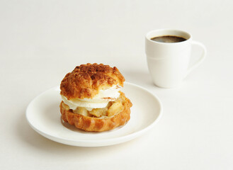 Shu cake dessert with cream on a white plate and a cup of coffee. White background