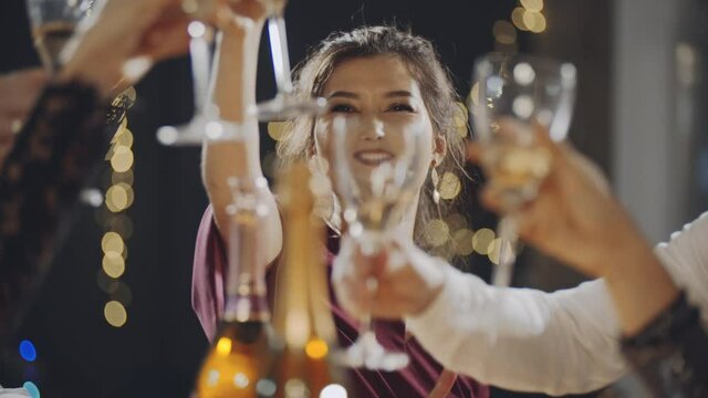 Close-up portrait of asian girl raising glass of champagne and clinking glasses with everyone at party or celebration. Brunette communicating or talking with friends and girlfriends at festive table.