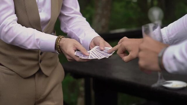 The magician shows a magic trick with playing cards. Male illusionist outdoor.