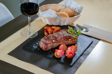 Churrasco chuletón de vaca al grill con copa de vino y guarnición de patatas fritas y tomates.