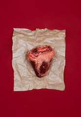Top view of real animal heart on a piece of craft paper and red background.
