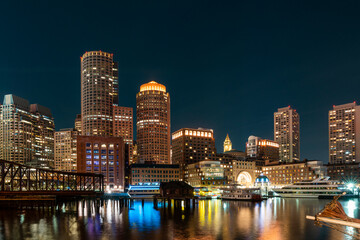 Fototapeta na wymiar Panoramic city view of Boston Harbour and Seaport Blvd at night time, Massachusetts. An intellectual, technological and political center. Building exteriors of financial downtown.