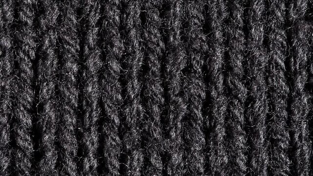 Knitted black fabric, thread knots close-up, rotating, macro, top view.