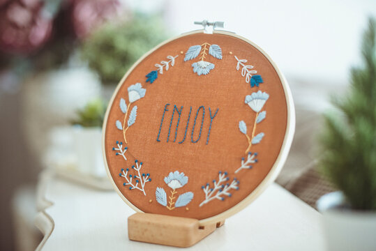 Embroidery hoop with the word enjoy on a sideboard with plants