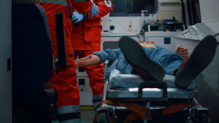 EMS paramedics treating patient with wound on hand in emergency car