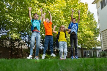 Group of funny excited children in school outdoor with backpacks and copybooks having fun and jumping