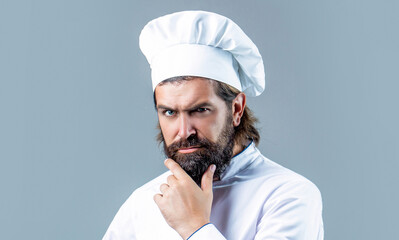 Serious cook in white uniform, chef hat. Portrait of a serious chef cook. Bearded chef, cooks or...
