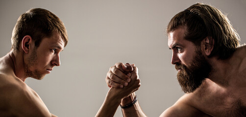 Arms wrestling thin hand, big strong arm in studio. Two man's hands clasped arm wrestling, strong and weak, unequal match. Heavily muscled bearded man arm wrestling a puny weak man