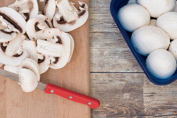 Champiñones enteros y en rodajas, en una tabla de cortar, un cuchillo rojo, vista superior