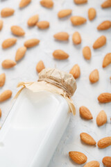 Vegan Milk from organic almonds in a glass bottle around a scattering of seeds on a light background.