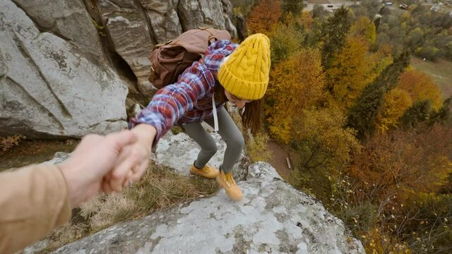 Closeup of male's hand stretching out and helping female hiker reach cliff top by pulling her up from edge. POV of man giving hand to woman climbing on cliff and helping her reach top. autumn hike.