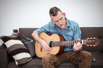 man in his 50s sitting on couch and playing guitar