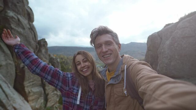 hikers hipstres man and woman on amazing landscape with cliffs in national park, rocks mountains and sunset sky on background. couple bloggers taking selfie or video call, huggs and kisses..