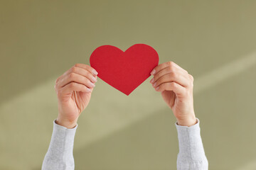 Close up of young woman's hands holding red paper heart as sign of blog likes, sympathy or approval...