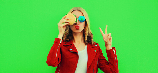 Portrait of stylish young woman eating tasty big burger fast food on green colorful background