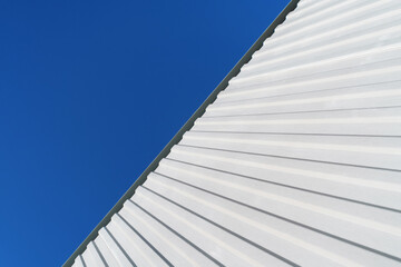 Geometry of a white corrugated metal building against a blue sky.