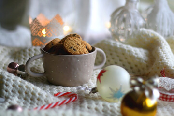 Bowl of cookies, soft knitted blanket and colorful Christmas ornaments at home. Selective focus. 