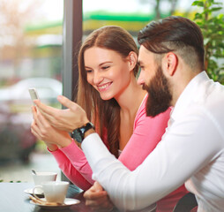Young happy couple in cafe having fun, chatting and taking selfies together