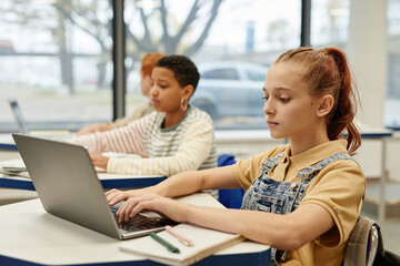 Side view portrait of diverse group of children in row using laptops in coding class, copy space