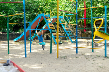 A little boy hangs on an iron bar. A boy is playing on an empty playground
