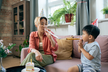 Young mother and cute little son blowing air whistles while having fun on birthday party at home