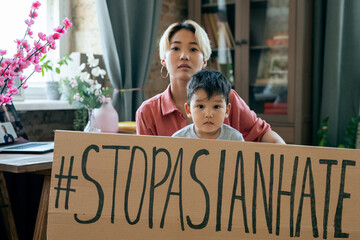 Young Asian woman and her little son holding slogan against national hate and ethnic dicrimination...