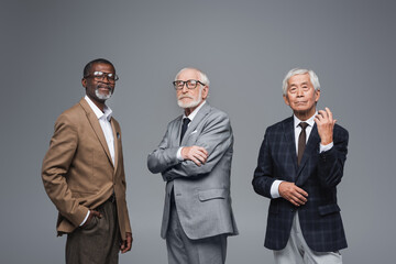 elderly multiethnic business partners in formal wear looking at camera while standing isolated on...