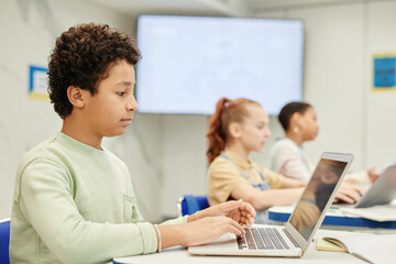 Side view portrait of teenage boy using laptop in coding class for children, copy space